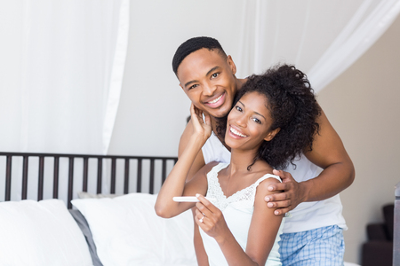 Portrait of happy couple with pregnancy test on bed in bedroomの写真素材