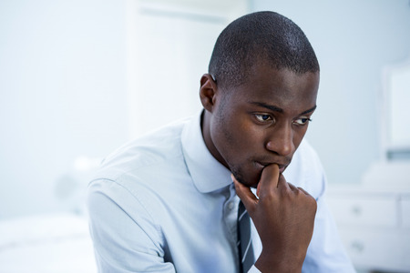 Thoughtful businessman sitting on bed in bedroomの写真素材