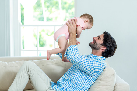 Father smiling while playing with son on sofa at homeの写真素材