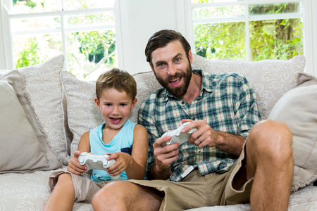 Portrait of father and son playing video game on sofa at home