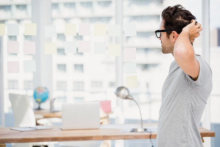 Thoughtful man looking at sticky notes on window in the officeの写真素材
