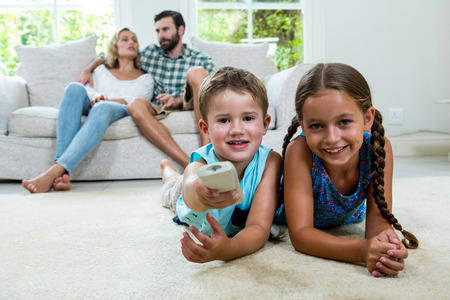 Portrait of happy siblings watching tv against parents relaxing at homeの写真素材