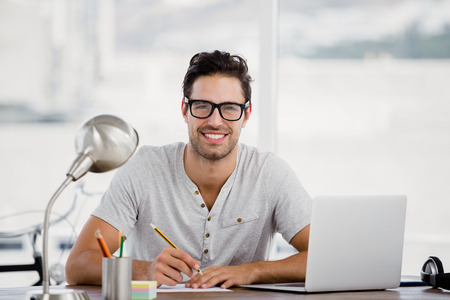 Portrait of young man working at his desk in the officeの写真素材