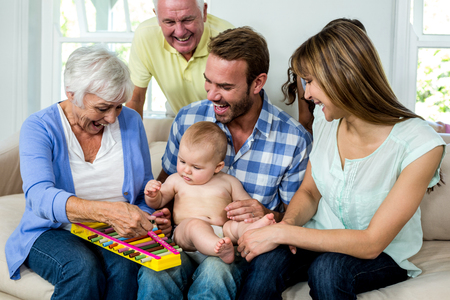 Happy multi-generation family showing xylophone to baby boy on sofa