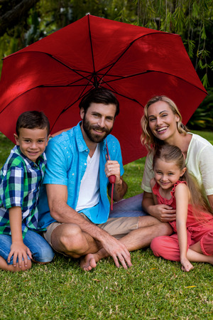 Portrait of smiling family sitting with umbrella in yardの写真素材