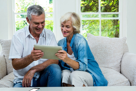 Happy senior couple holding digital tablet in sitting room at homeの写真素材