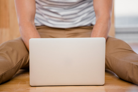 Mid-section of man sitting on the floor and using laptop at home