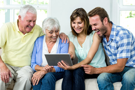 Family laughing while looking in digital tablet at homeの写真素材