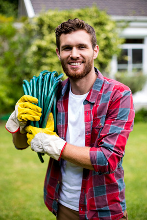 Portrait of smiling man carrying garden hose in yardの写真素材