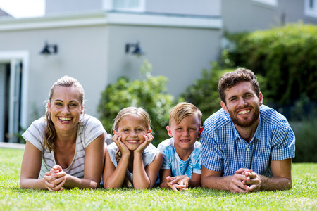 Front view of happy family lying on grass in yardの写真素材