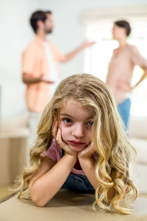 Close-up portrait of upset girl leaning on box while parents arguing in backgroundの写真素材