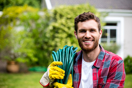 Smiling man carrying garden hose while standing in backyard