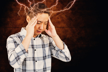 Asian man getting a headache against dark fenceの写真素材