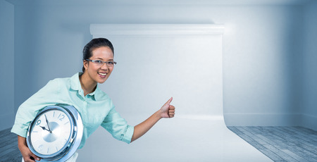Delighted businesswoman holding a clock against large white screen