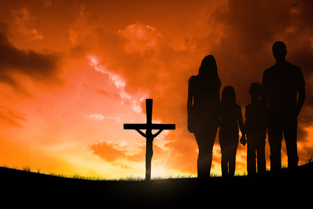 Cheerful family holding hands against cross religion symbol shape over sunset skyの写真素材