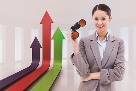 Portrait of a businesswoman holding binoculars against bright room with windowsの写真素材