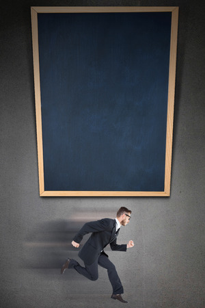 Geeky young businessman running mid air on black background with a black boardの写真素材
