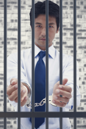 Portrait of a businessman with handcuffs against grey brick wallの写真素材