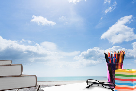 School supplies on desk against beach with blue skyの写真素材