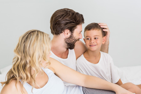 Parents and son sitting on bed in bedroom at homeの写真素材