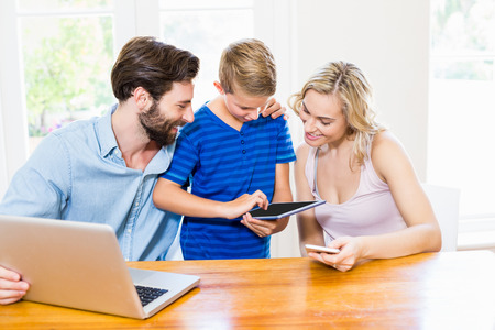 Parents and son using a laptop, tablet and phone at homeの写真素材