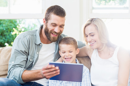 Happy family sitting on sofa using digital tablet in living roomの写真素材