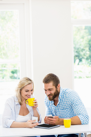 Couple using mobile phone while having coffee at homeの写真素材