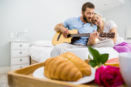 Man playing guitar for woman in bed at bedroomの写真素材