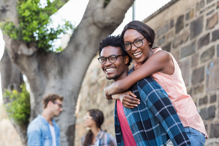 Portrait of young man giving piggyback to woman with friend backgroundの写真素材
