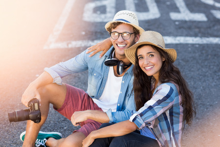 Portrait of happy young couple in hat sitting on roadの写真素材