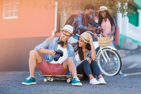 Couple sitting on road interacting while their friends standing in backgroundの写真素材