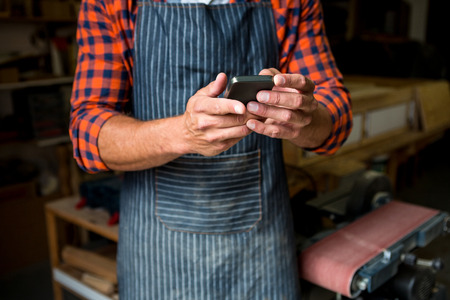Carpenter is looking at his phone in a dusty workshopの写真素材