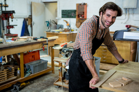 Carpenter is posing with his craft in a dusty workshop