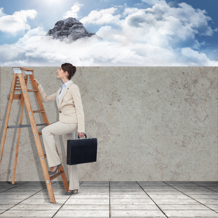 Businessman looking on a ladder against mountain peak through the cloudsの写真素材
