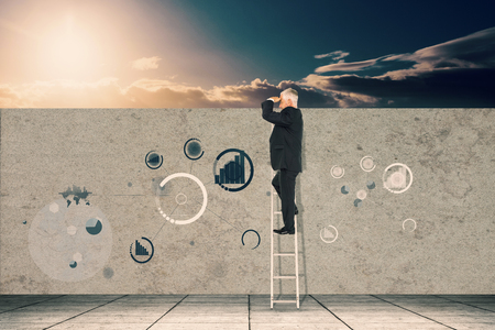 Mature businessman standing on ladder against a beautiful sunset on a beachの写真素材