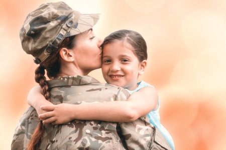 Close-up of mother in army uniform kissing daughter against colorful backgroundの写真素材