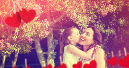 Composite image of mother and daughter holding each other in garden behind heart tinselの写真素材