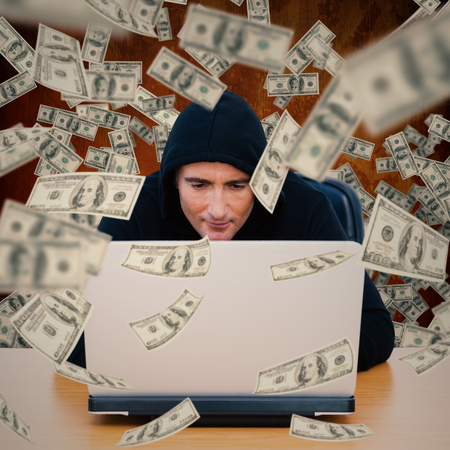 Smiling thief in hood jacket using laptop and credit card against brown paint splashed surface