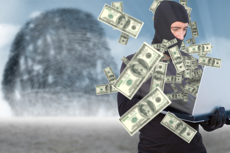 Burglar with balaclava hacking a laptop against thumbprint graphic over desertの写真素材