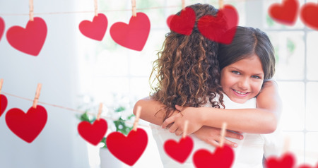 Composite image of mother and daughter holding each other behind heart tinselの写真素材