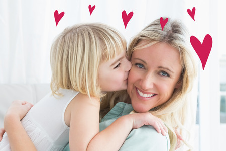 Red Hearts against mother sitting on the couch with her daughter kissing her cheekの写真素材