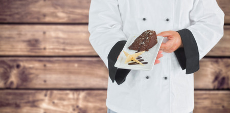 Close up on a chef holding a chocolate cake against wooden planks backgroundの写真素材