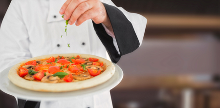Close up on a chef holding a pizza against pots and pans on stove topの写真素材