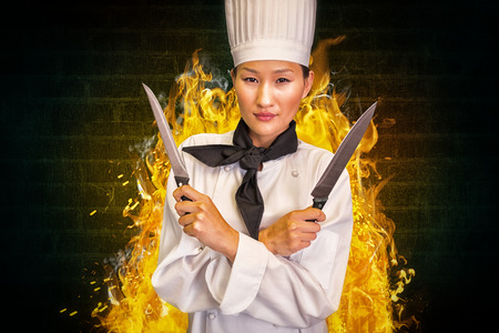 Confident female cook holding knives in kitchen against green background with vignetteの写真素材