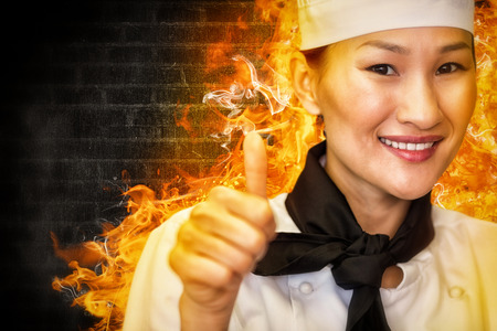 Portrait of smiling female cook gesturing thumbs up against a dark wall