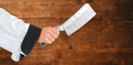 Composite image of chef hand holding a knife against a wooden backgroundの写真素材