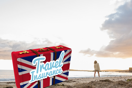 Woman in sweater walking on beach against travel insurance message on a british suitcaseの写真素材