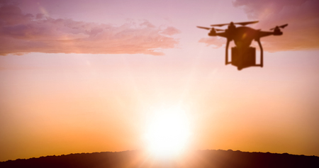 A drone bringing a red cube against sun shiningの写真素材