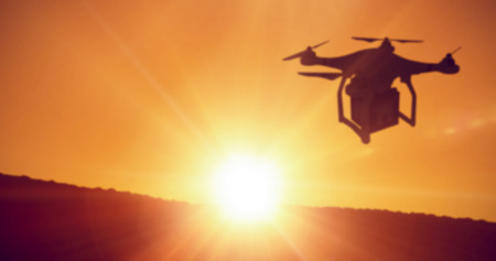 A drone bringing a purple cube against sun settingの写真素材