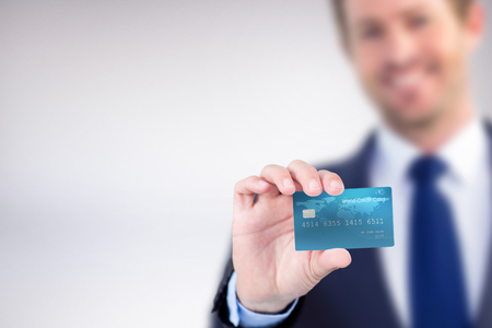 Happy businessman showing a creditcard against grey backgroundの写真素材